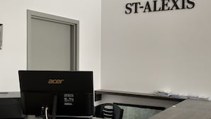 Ein Hotelrezeptionstresen mit einem Laptop, einem Drucker und einem Wandzeichen mit der Aufschrift 'HOTEL ST-ALEXIS'.