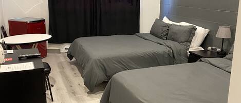 A modern bedroom with two beds, a desk, a chair, and a red appliance.