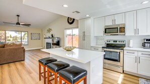 A modern kitchen with white cabinets, a large island with stools, stainless steel appliances, and a ceiling fan.