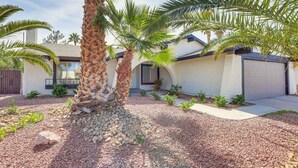 A modern house with a well-maintained garden, including palm trees and a gravel driveway.