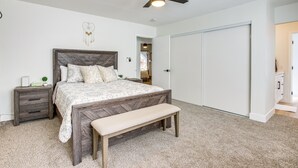 A bedroom with a bed, a bench, a nightstand, a ceiling fan, and a wardrobe.