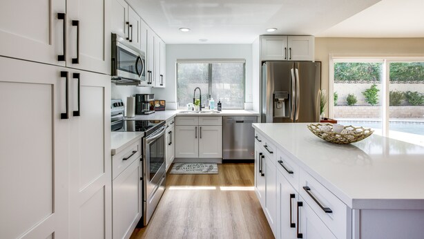 A modern kitchen with white cabinetry, stainless steel appliances, and a large window providing natural light.