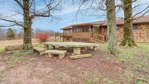 Un edificio de piedra con una terraza de madera y una mesa de picnic en un área boscosa.