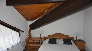 A bedroom with a wooden bed, two bedside tables with lamps, a wooden nightstand, a window with white curtains, and a wooden ceiling beam. - 1st floor, balcony, tv, 44m², Pralognan-la-Vanoise (Pralognan-la-Vanoise)