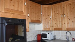 A kitchen with wooden cabinets, a black oven, a white microwave, and a red coffee maker. - 1st floor, balcony, tv, 44m², Pralognan-la-Vanoise (Pralognan-la-Vanoise)