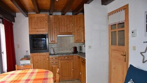 A compact kitchen with wooden cabinets, a microwave, and a stove. There is a bed with a colorful blanket and a pillow with a leaf pattern. - 1st floor, balcony, tv, 44m², Pralognan-la-Vanoise (Pralognan-la-Vanoise)