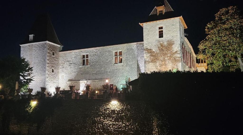 A stone castle with a moat, illuminated by lights at night.