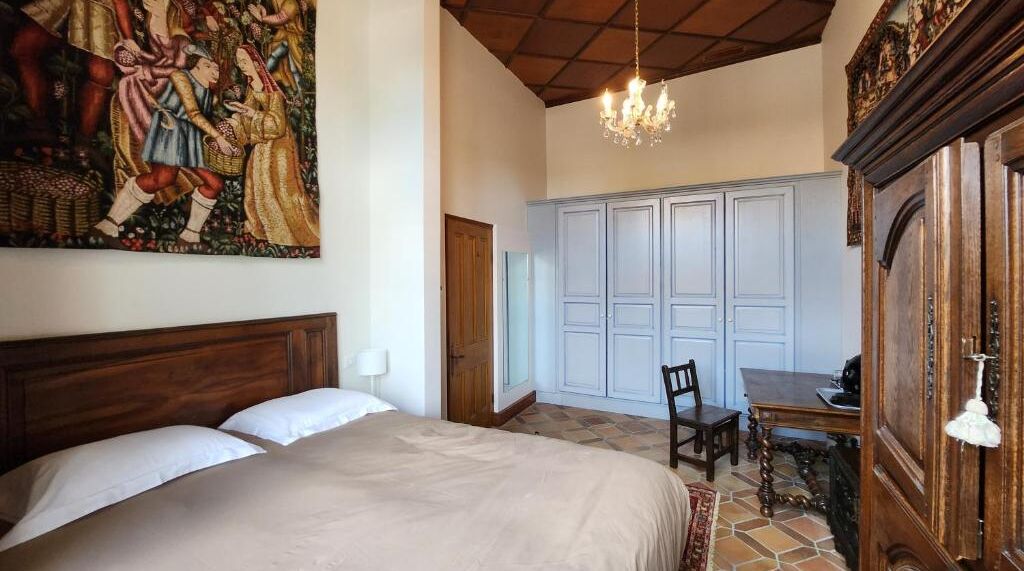 Een slaapkamer met een groot bed, een houten hoofdbord, een kroonluchter, een eettafel met stoelen en een garderobe.