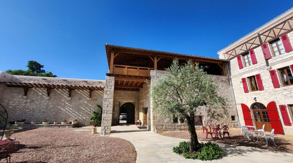 A courtyard with stone buildings, a covered wooden structure, and outdoor seating.