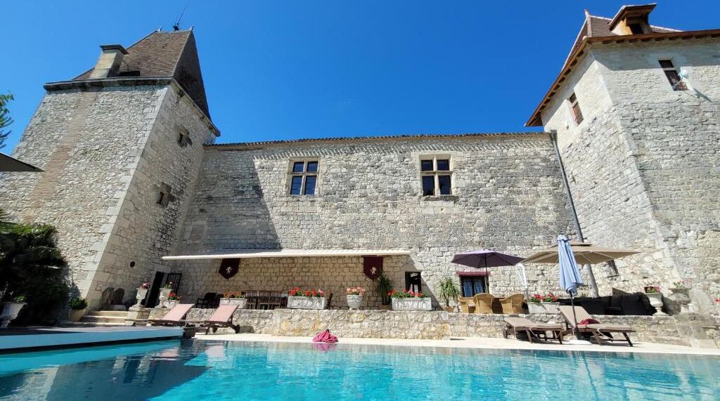Un edificio de piedra con piscina y sillones de descanso.