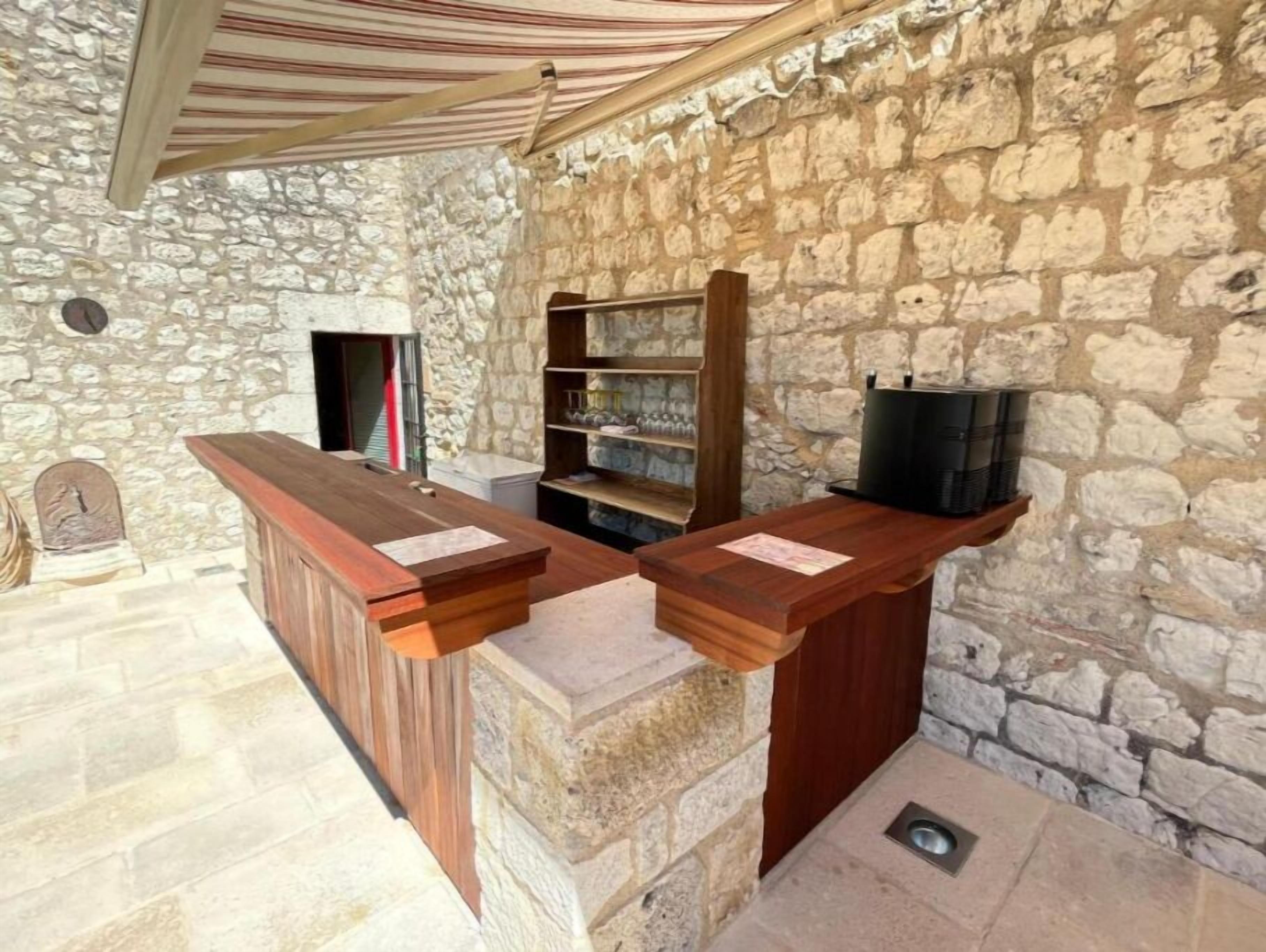 Una habitación con paredes de piedra, un mostrador de recepción de madera y una estantería con vasos.