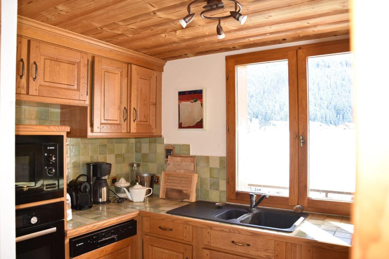 A kitchen with wooden cabinets, a coffee maker, a kettle, and a sink.