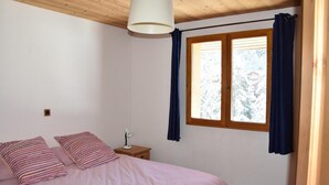 Un dormitorio con cama, mesita de noche, lámpara y ventana con cortinas.