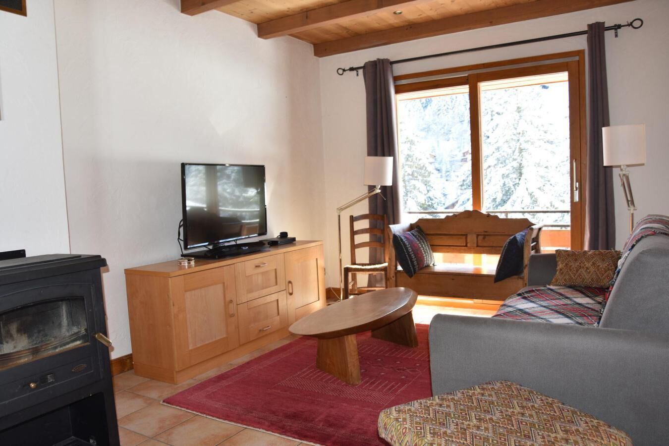 A cozy living room with a television, wooden furniture, a sofa, and a window with curtains.