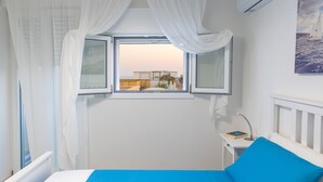 A bedroom with a bed, a window with curtains, a bedside table with a lamp, and a wall-mounted air conditioner.