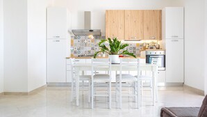 A modern kitchen with white cabinetry, a central island with chairs, and a potted plant.