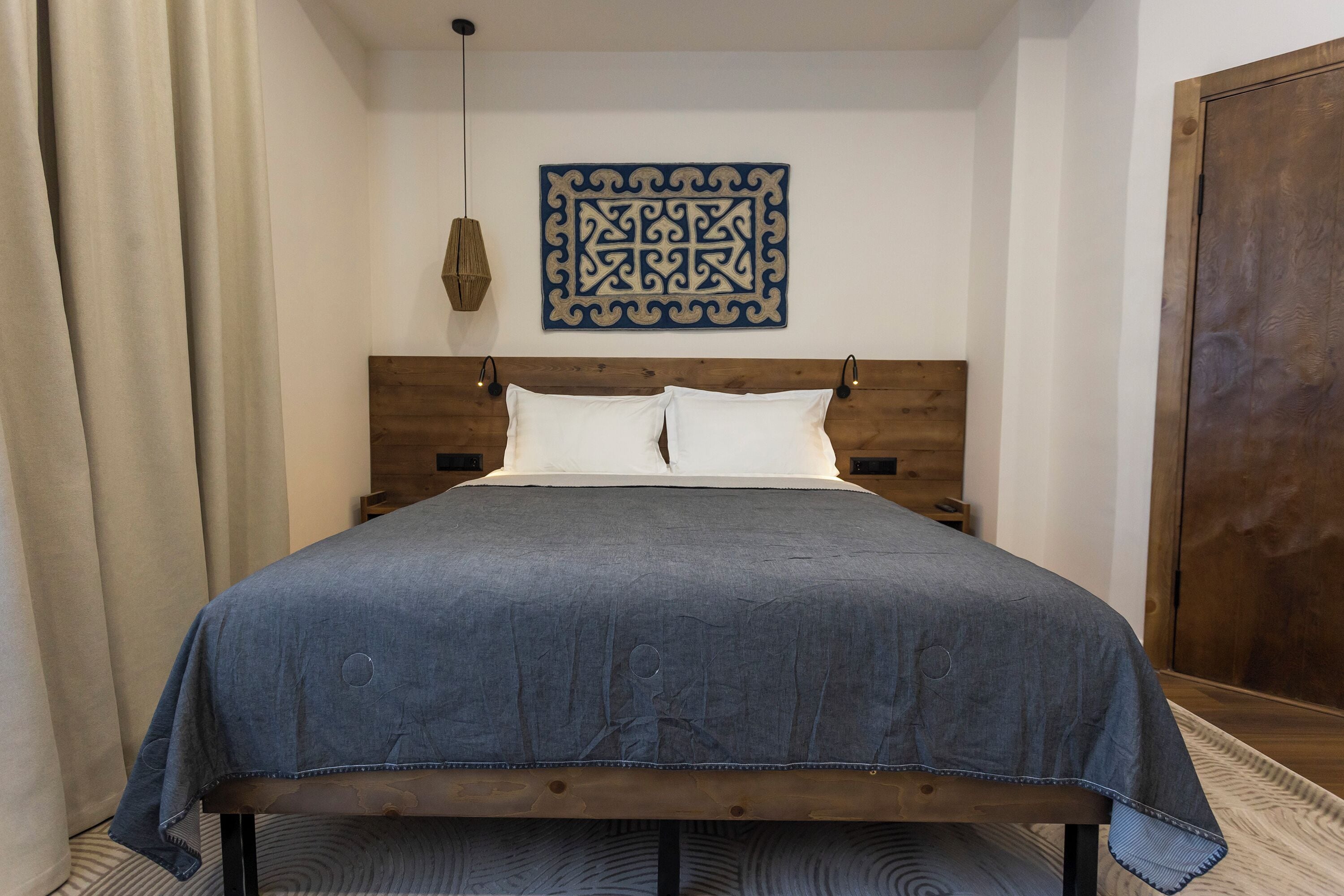 A neatly made bed with a wooden headboard, white pillows, and a blue bedspread.