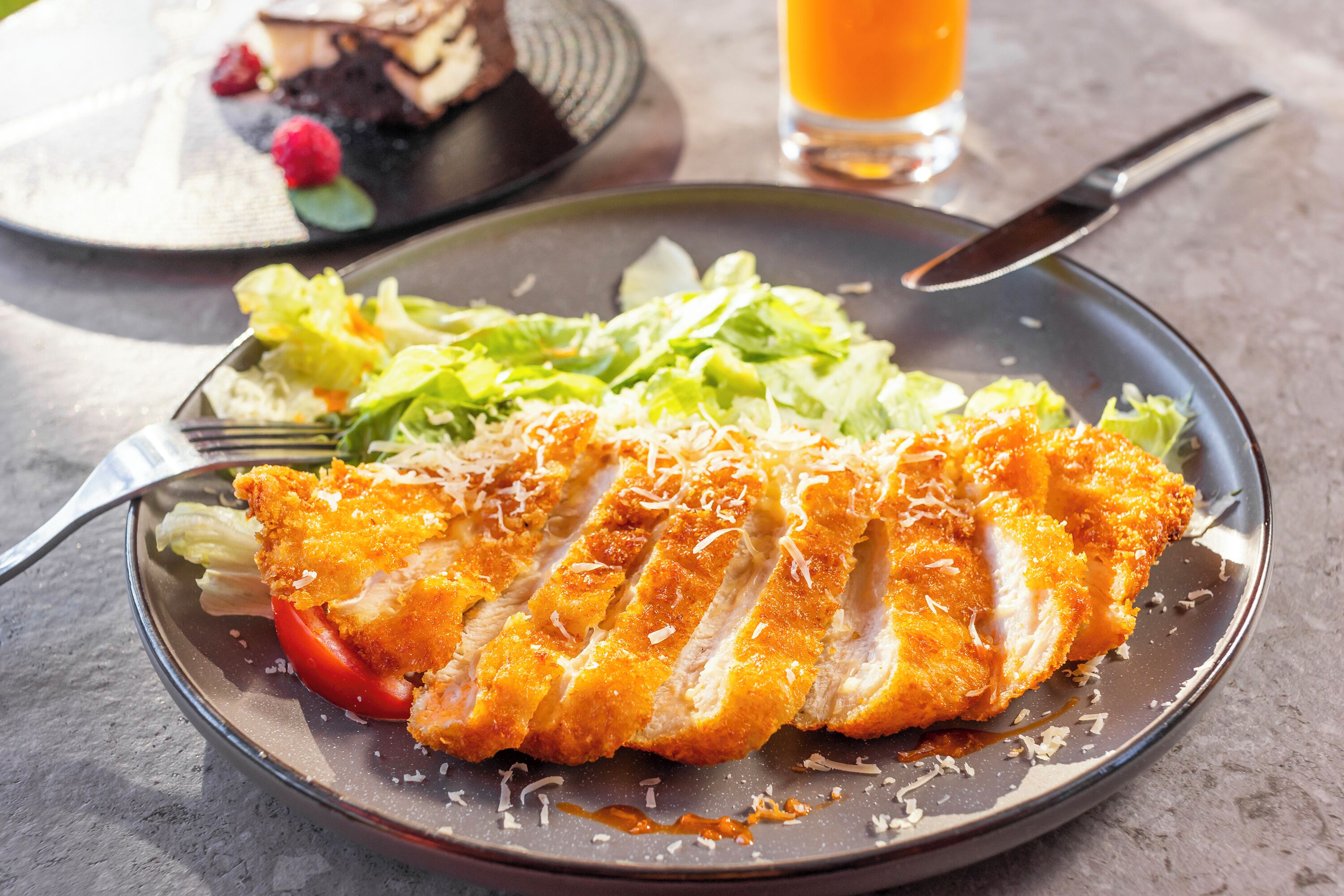 Une assiette contenant du poulet pané, une salade et un verre de jus d’orange.