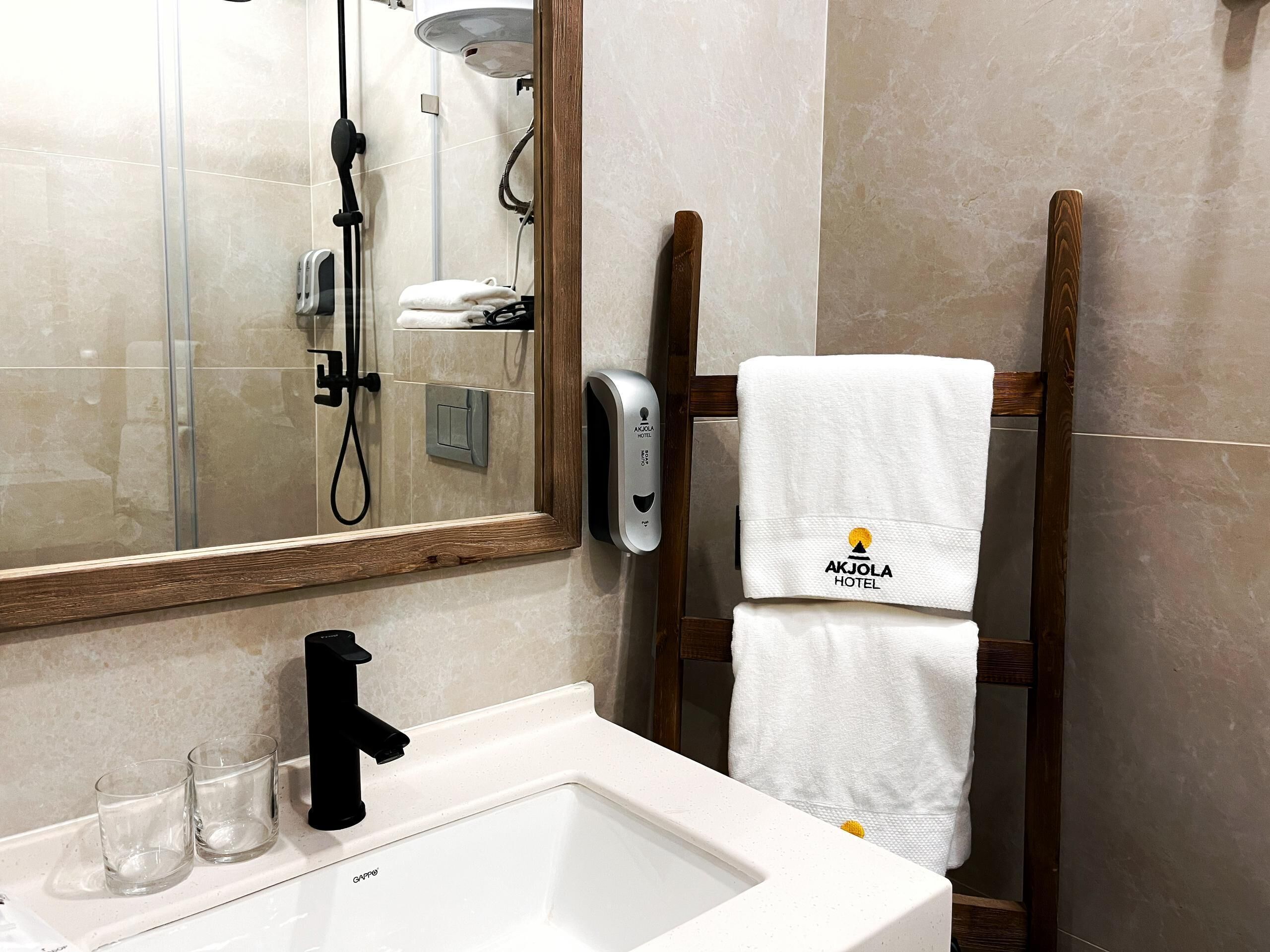 A bathroom with a large mirror, a sink, two glasses, a towel rack with a towel, and a shower area.