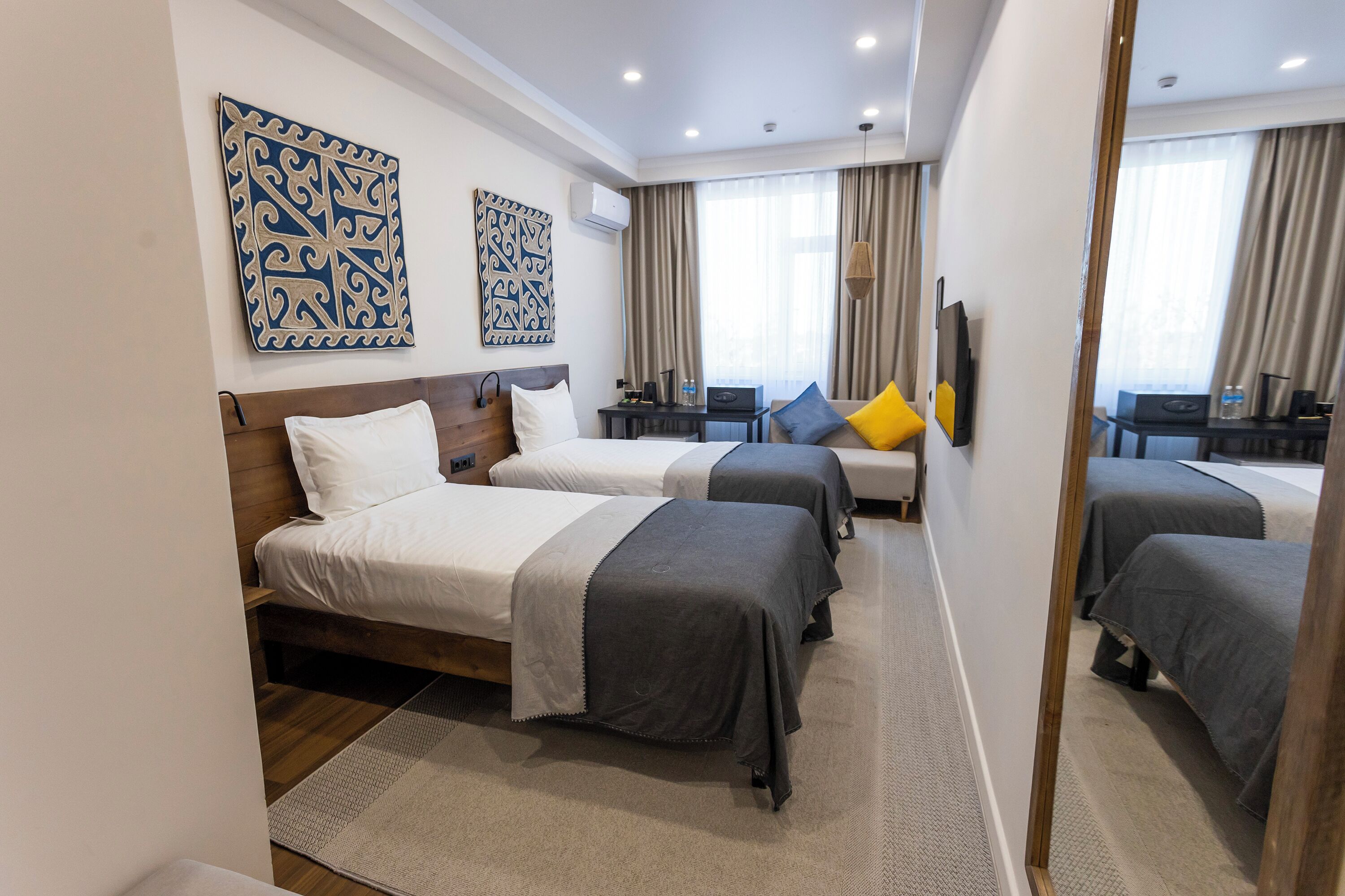 A hotel room with two beds, a desk, a chair, and a mirror.