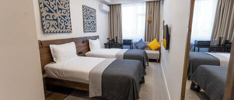 A hotel room with two beds, a desk, a chair, and a mirror.