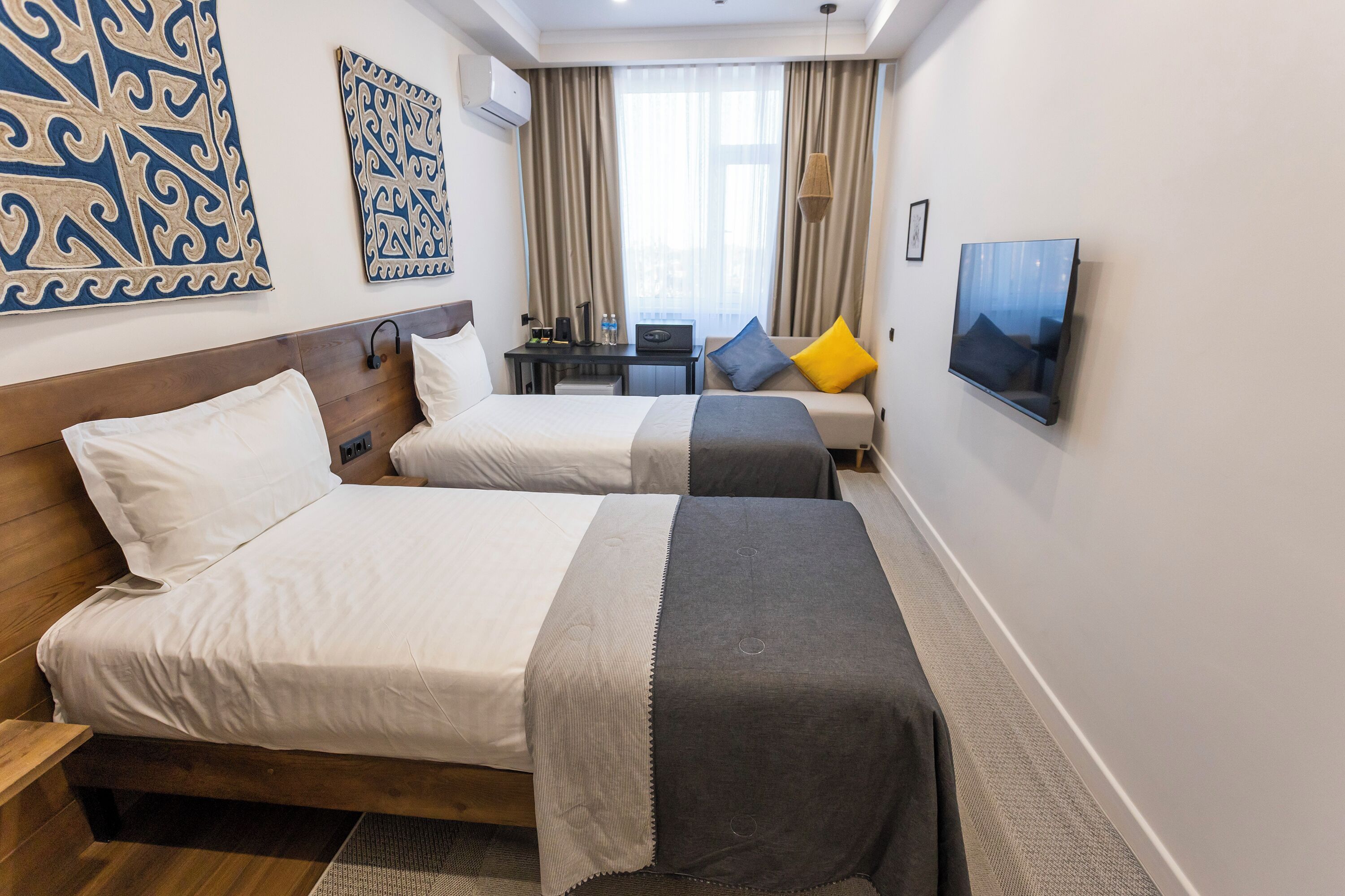 A hotel room with two beds, a desk, a TV, and artwork on the walls.