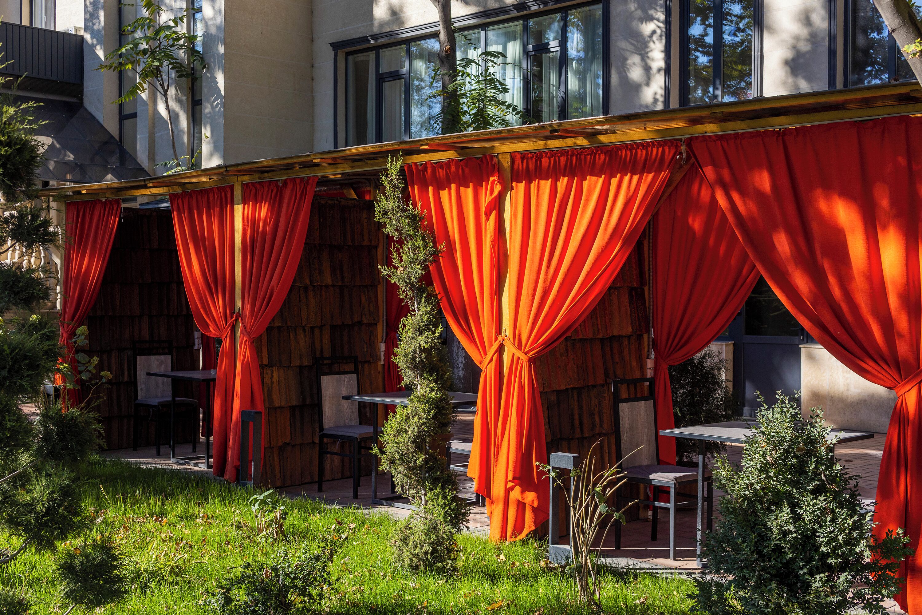 A covered outdoor seating area with red curtains, tables, and chairs.