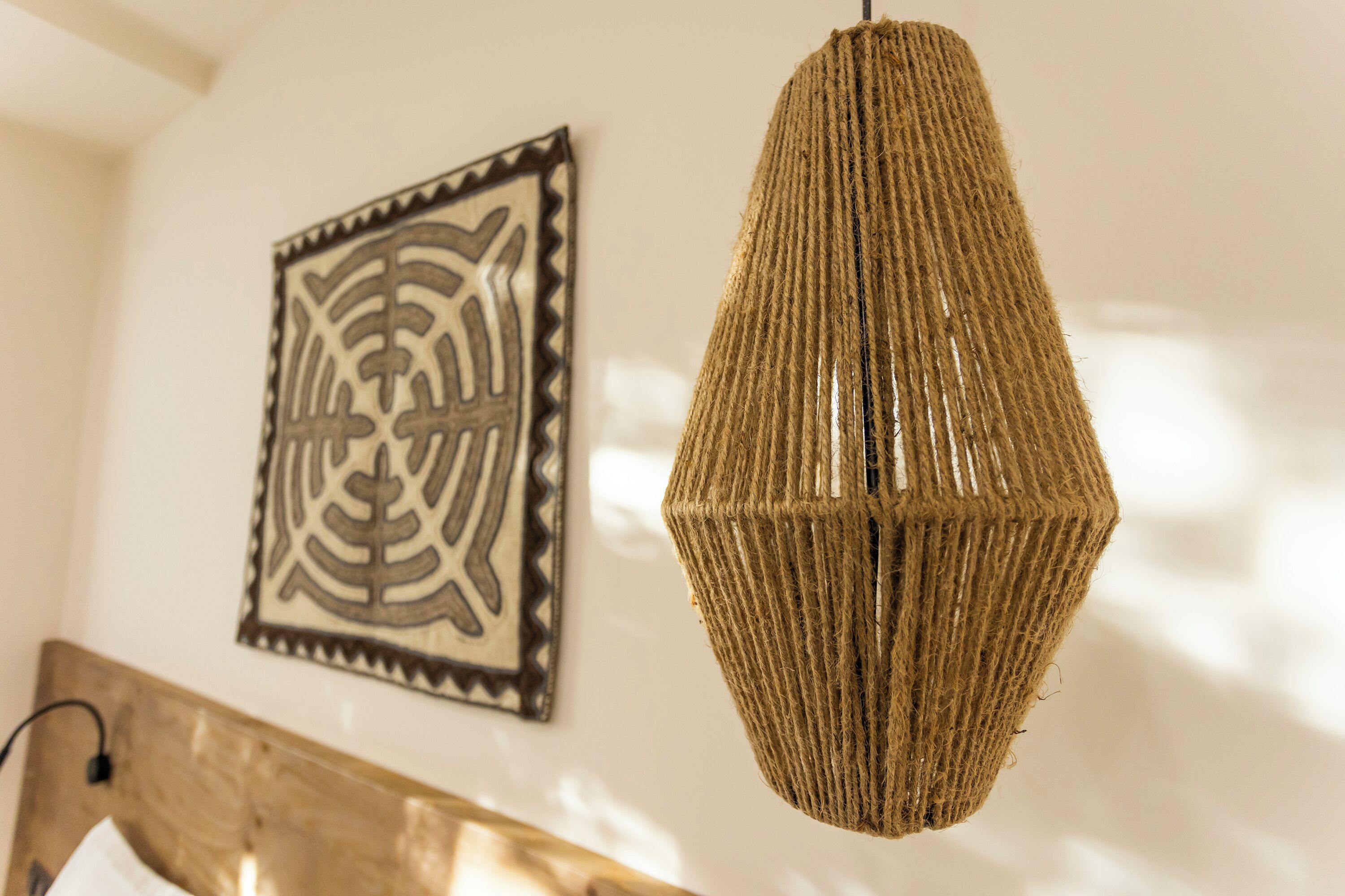 Una lámpara colgante tejida, suspendida del techo en una habitación con cabecera de madera y un adorno de pared.