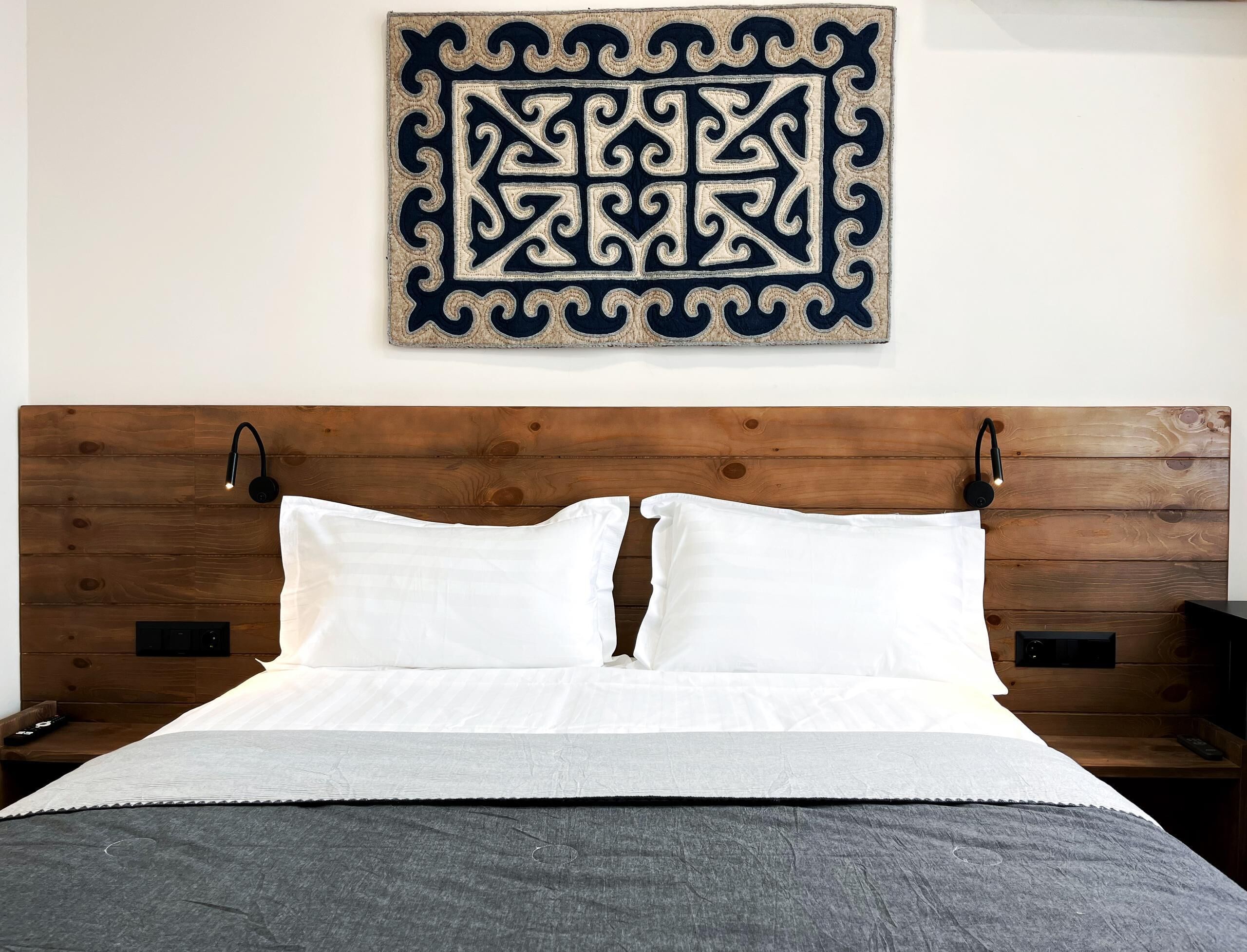 Un lit bien fait, avec du linge de lit blanc, une tête de lit sombre et un élément décoratif accroché au mur au-dessus.