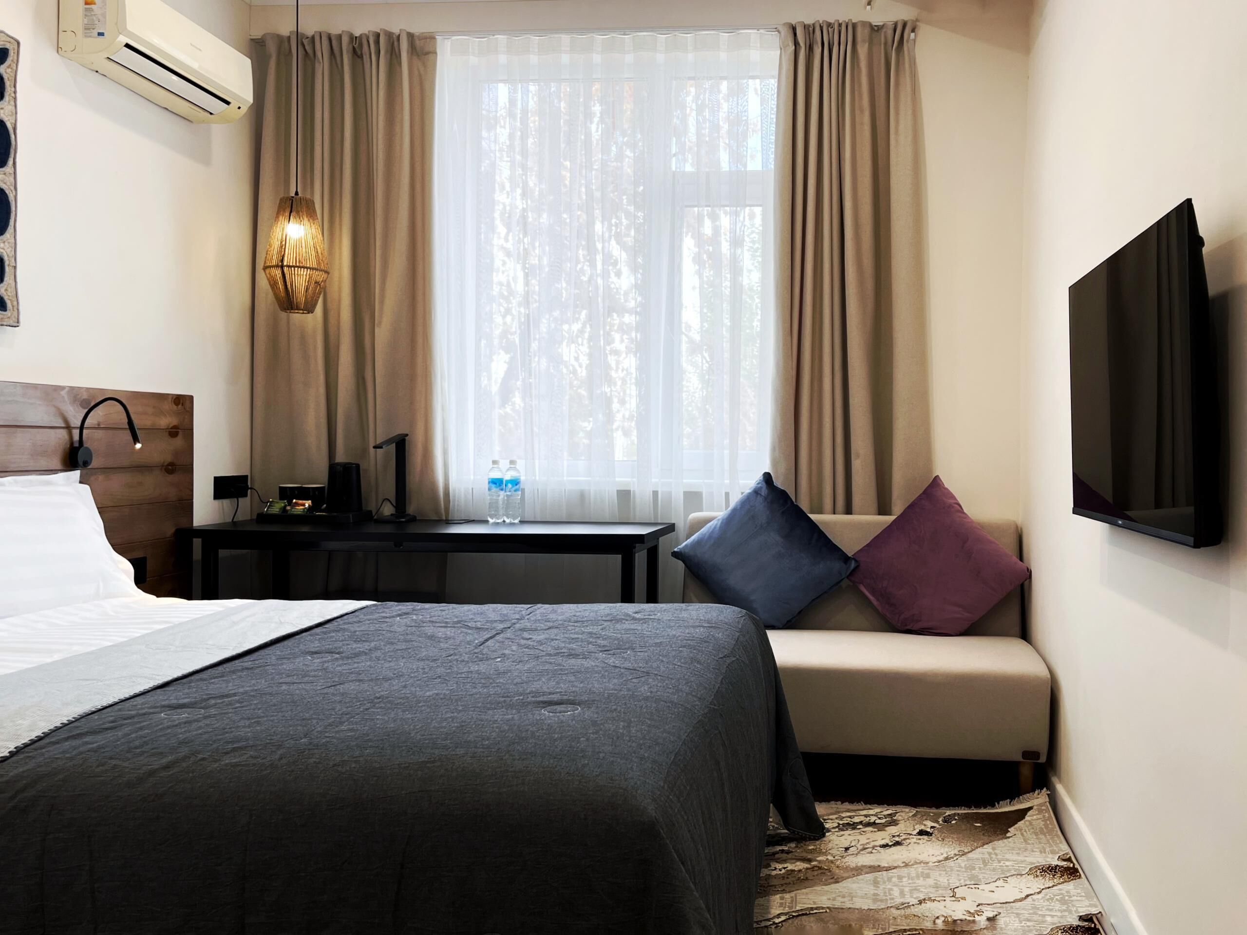 A hotel room with a bed, a desk, a chair, a television, and a window with curtains.