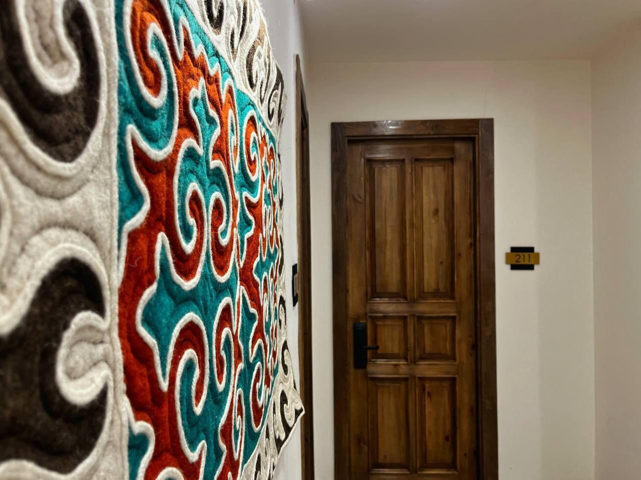 Un pasillo con una puerta de madera y un tapiz de colores.