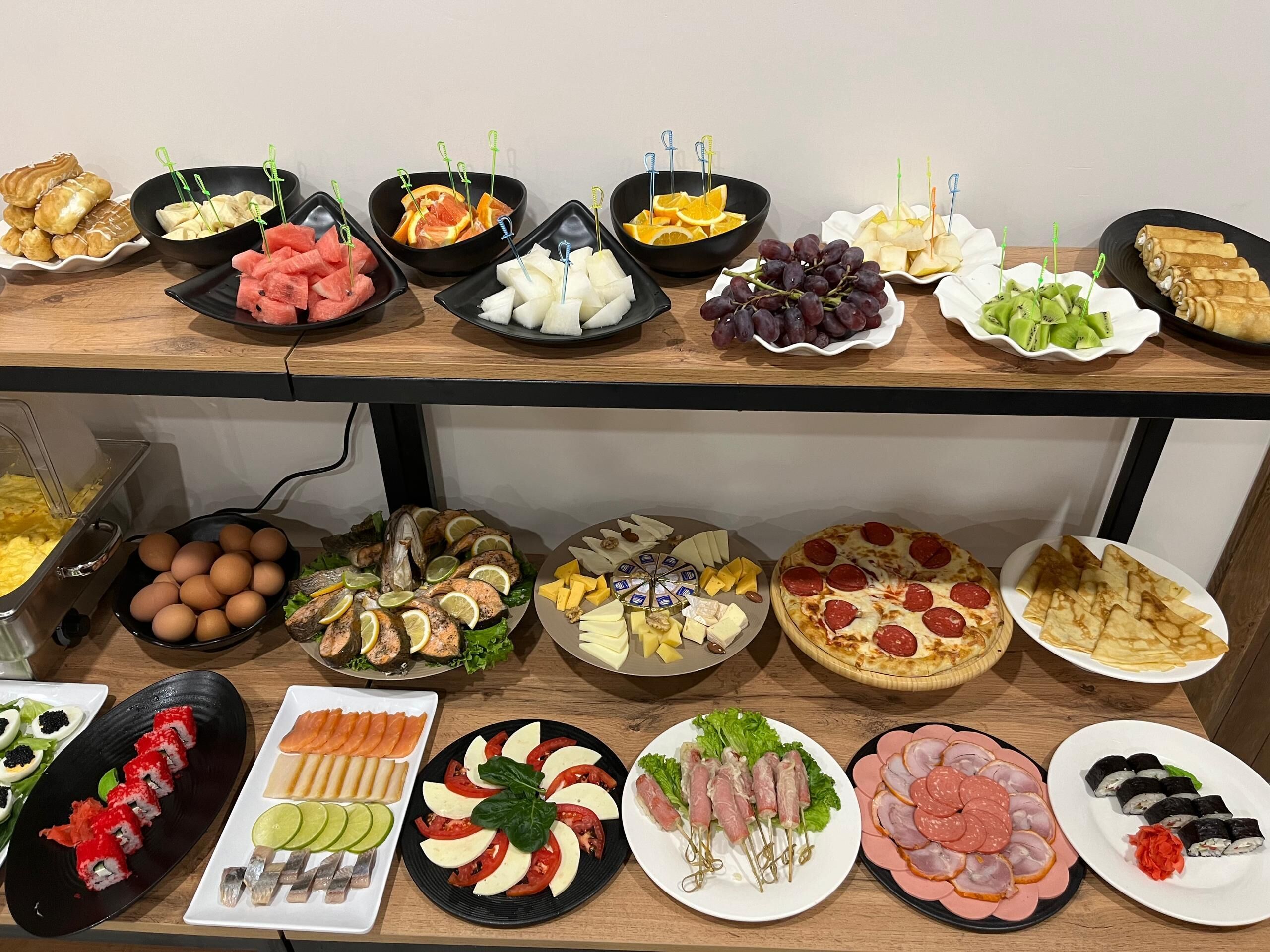 A buffet table with various food items including sushi, meats, cheeses, and fruits.