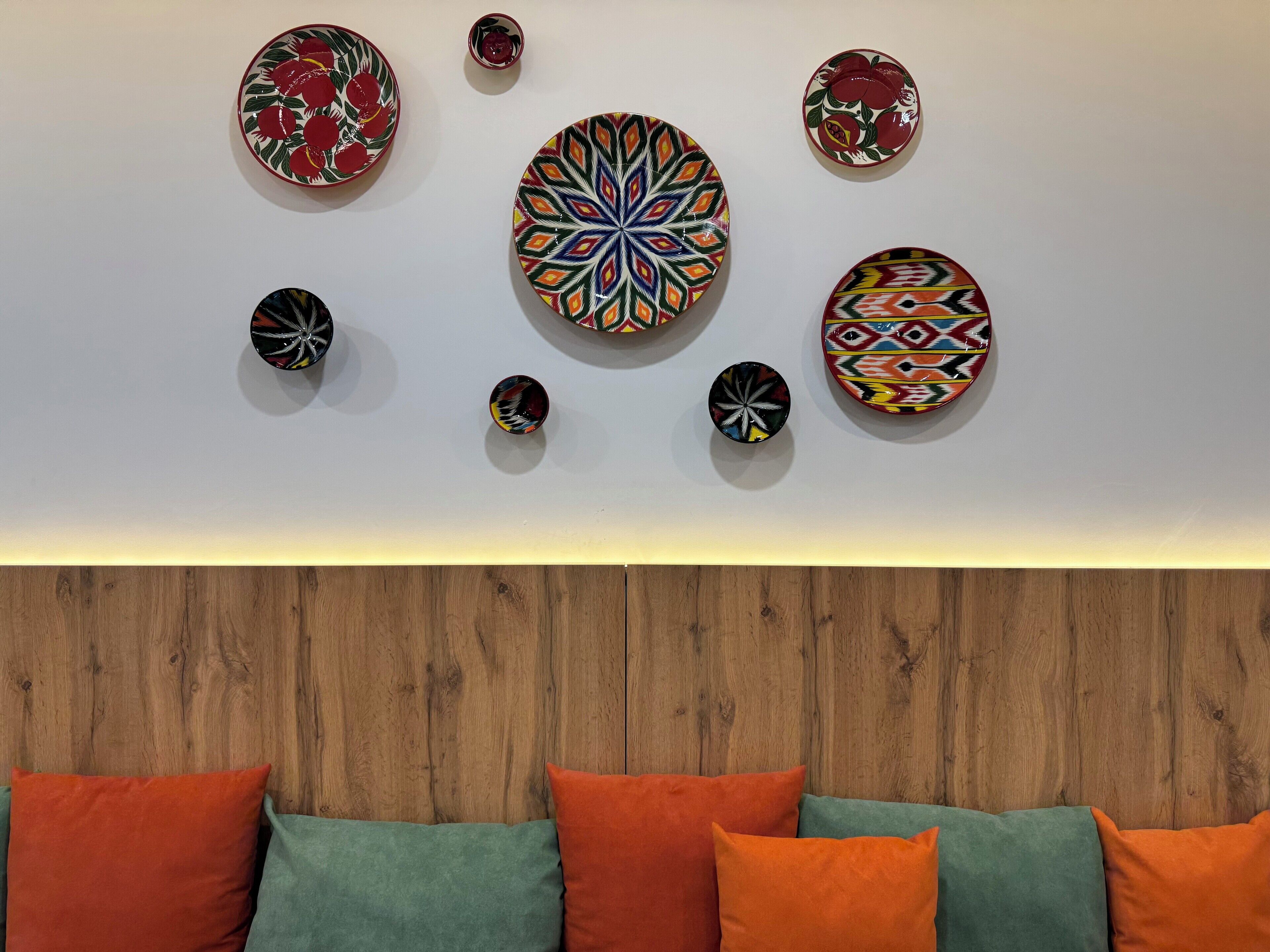 A room with a wooden headboard, a bed with orange and green pillows, and a wall decorated with various colorful plates.