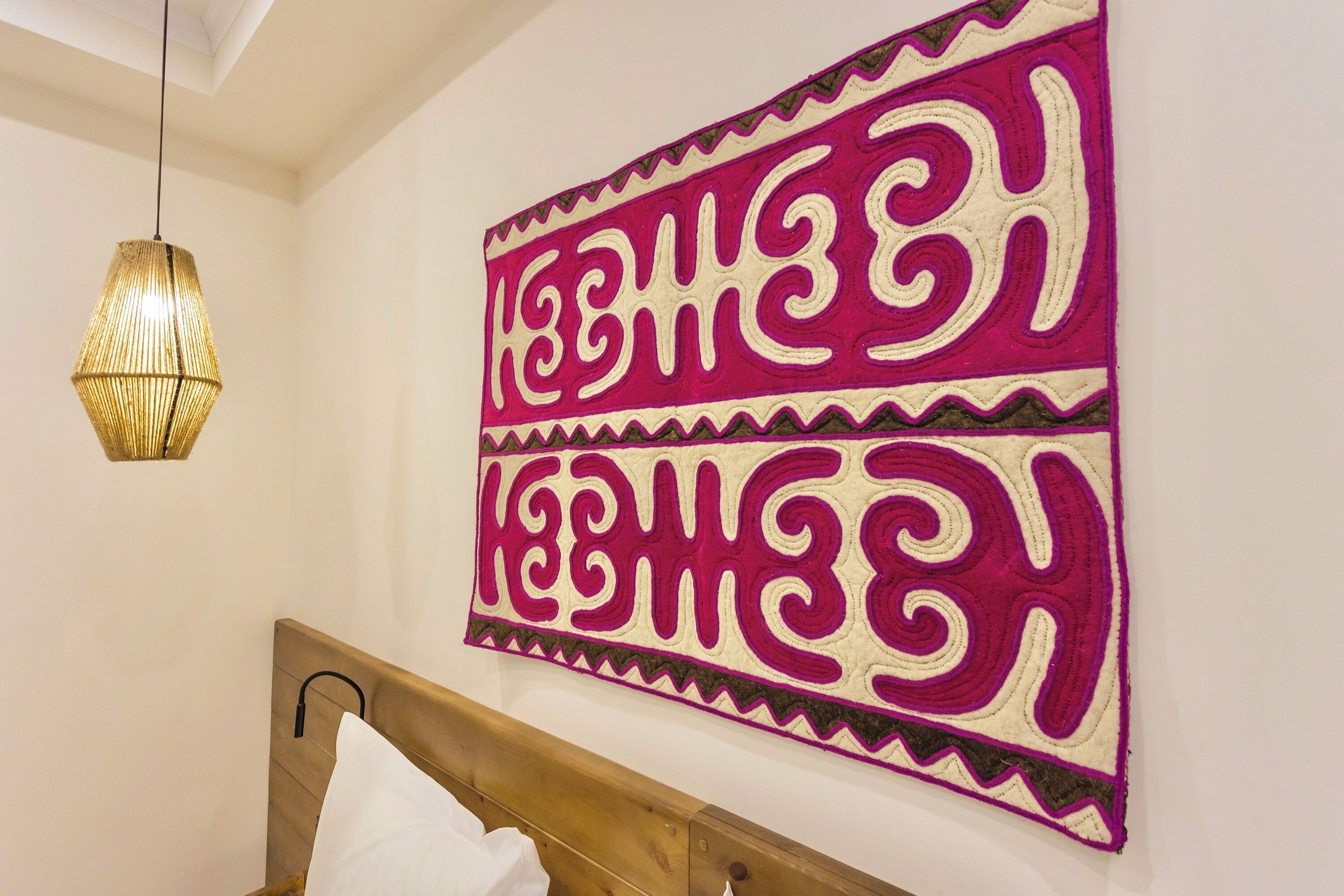 Une pièce comprenant un lit, un luminaire suspendu et un mur orné d’un textile décoratif.