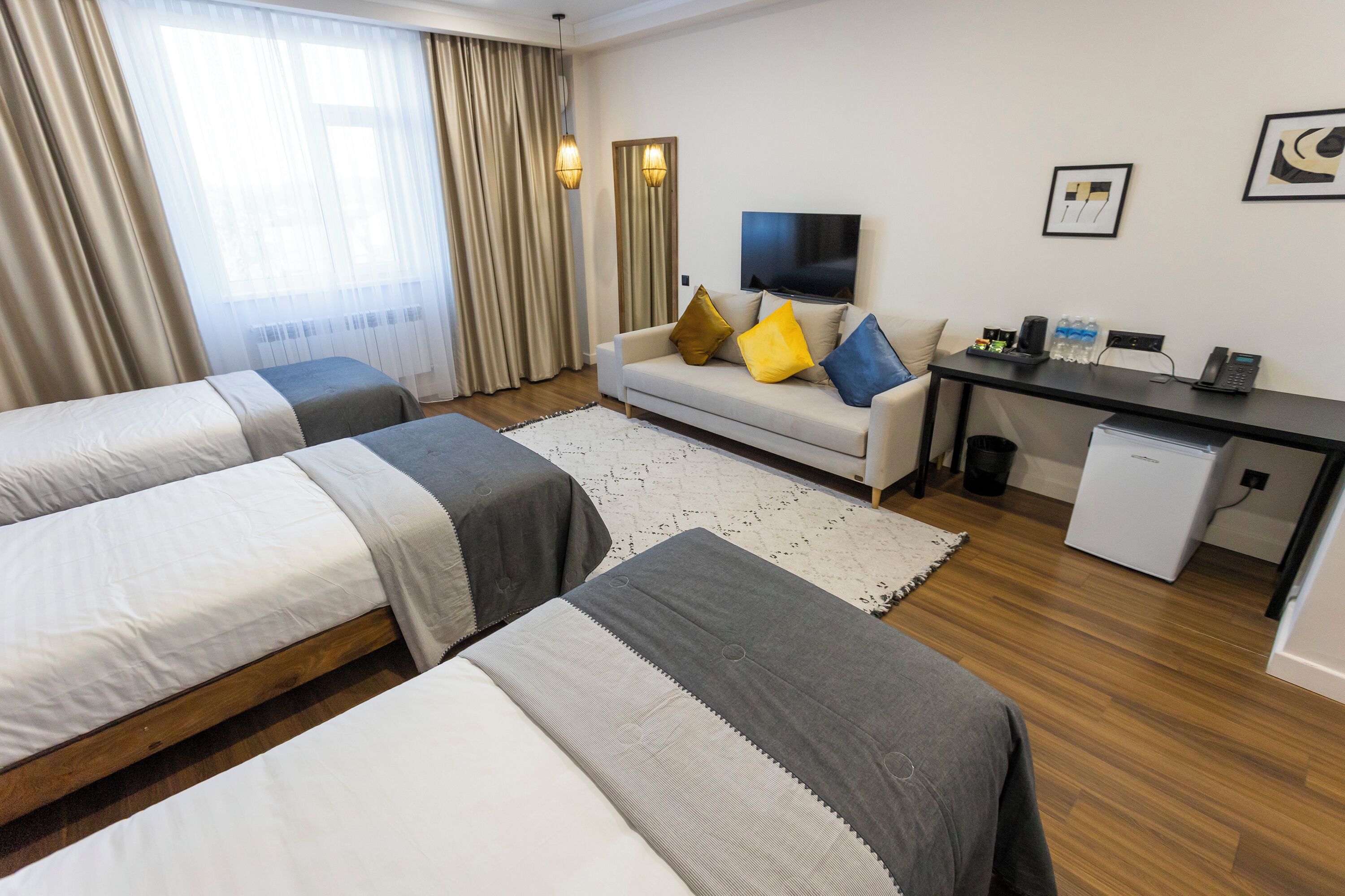 Ein Hotelzimmer mit zwei Einzelbetten, einer Couch, einem Schreibtisch mit Fernseher und einem kleinen Kühlschrank.