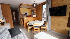 A cozy room with a bed, a dining table with chairs, a TV mounted on the wall, and a kitchen area in the background. - 50m from ski slopes, 4th floor, balcony, tv, 34m², Tignes (Tignes)