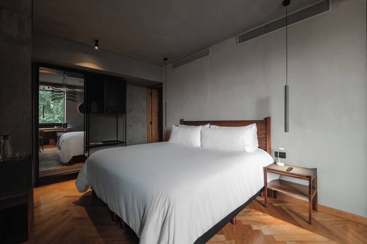 A modern bedroom with a large bed, a wooden nightstand, and a mirror.