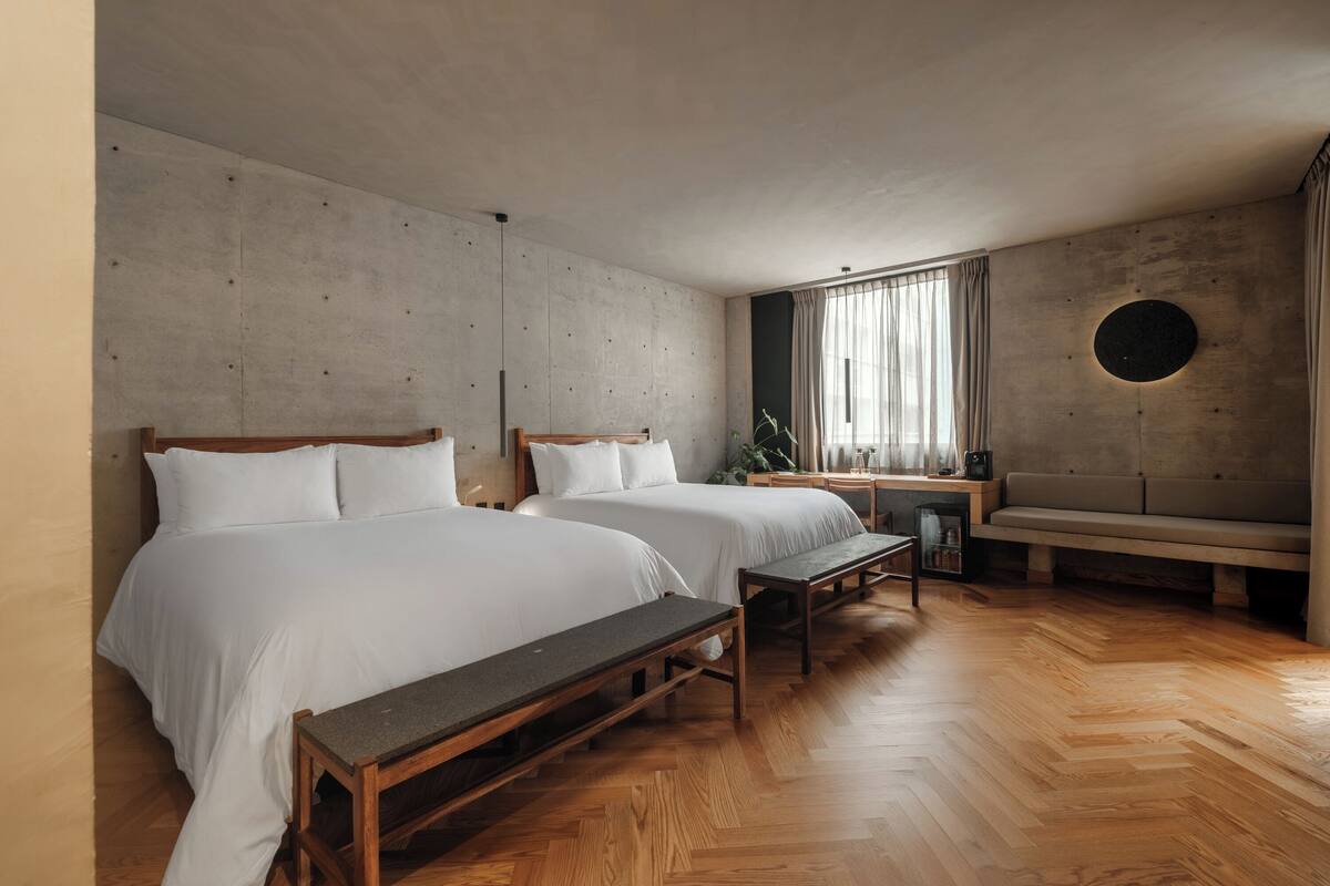 A modern bedroom with two beds, a bench, a desk, and a round wall decoration.