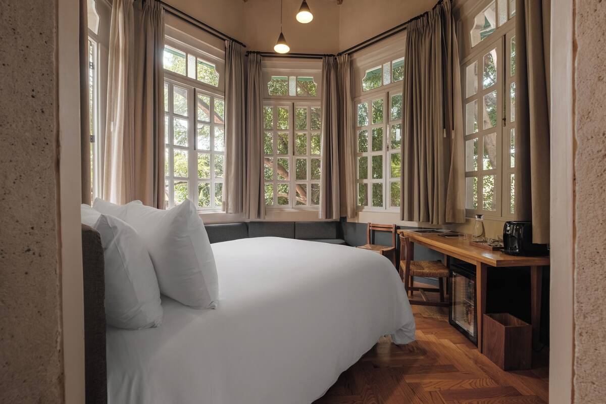 A bedroom with a large bed, a desk, and a view of trees through the windows.