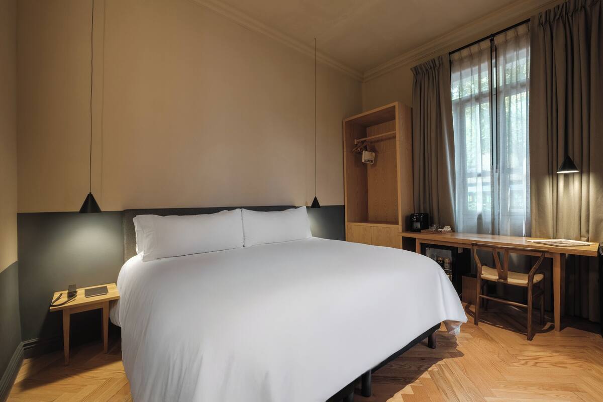 A bedroom with a large bed, a desk, a chair, and a wardrobe.