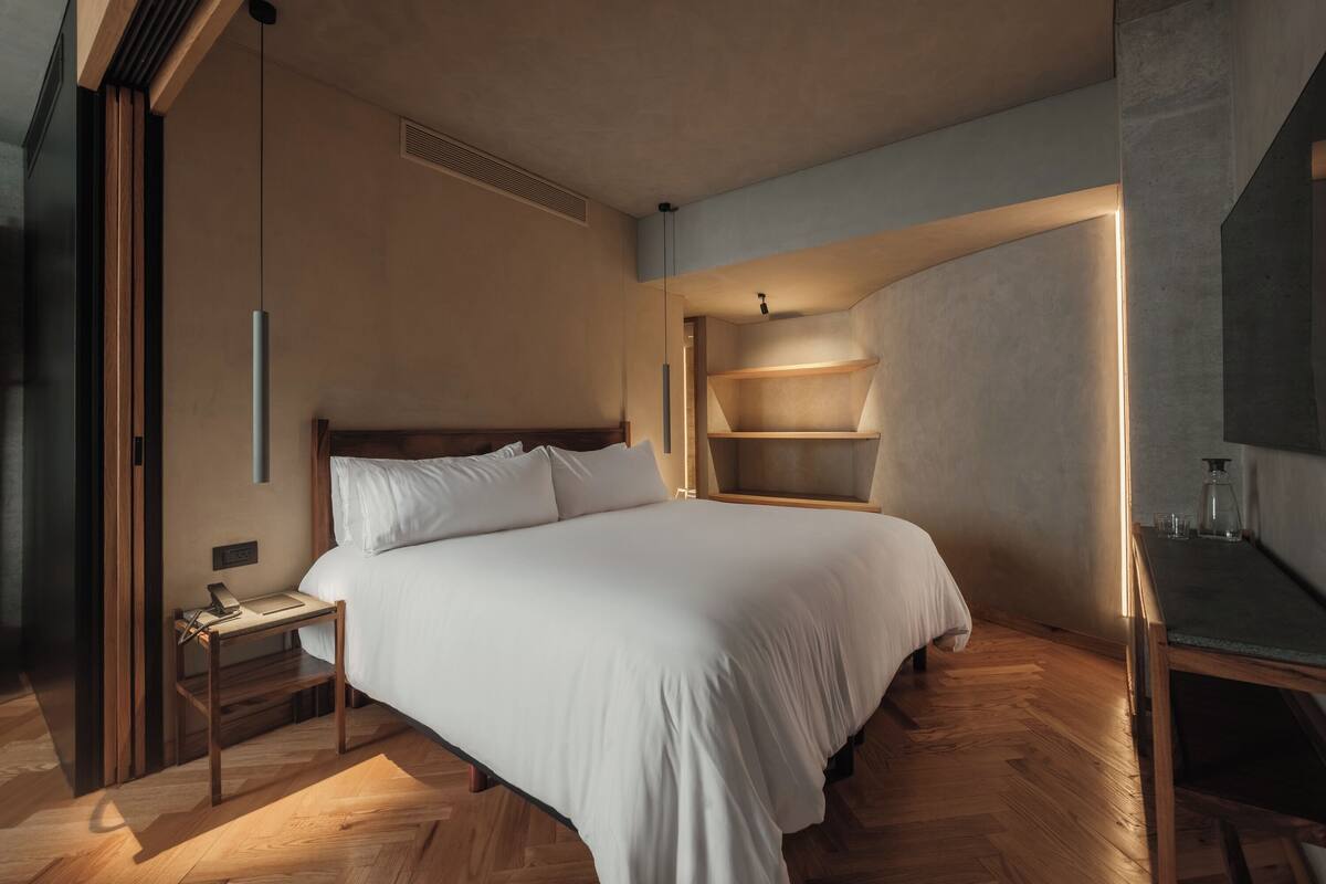 A modern bedroom with a large bed, wooden nightstand, and built-in shelving.