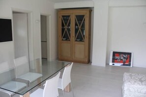 Un salon moderne avec une table à manger en verre, des chaises blanches, un meuble en bois et un tableau encadré accroché au mur.