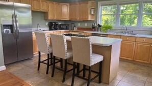 A kitchen with wooden cabinets, a stainless steel refrigerator, a microwave, a coffee maker, and a bar area with four chairs.