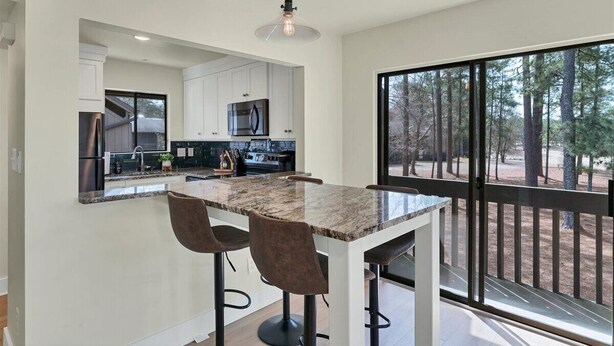 A modern kitchen with white cabinets, a granite countertop, and a bar area with stools. - Pick of the Pines Pinehurst (Pinehurst)