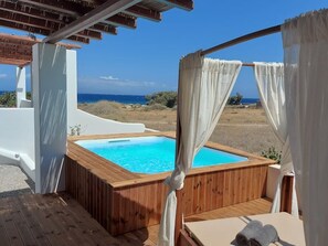Una vasca idromassaggio in legno con tende bianche, un pontile in legno e vista sul mare.