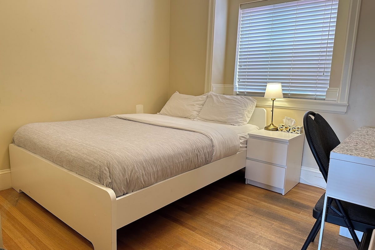 A bedroom with a bed, bedside table, lamp, and a chair.