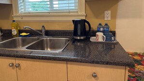 Una cocina con un lavamanos doble, una tetera y una encimera con una botella de detergente y botellas de agua.