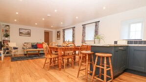A spacious living area with a wooden dining table, chairs, and a sofa. There is a kitchen area with a countertop and cabinets. - The Byre (Hexham)