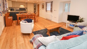 A modern apartment with a dining area, kitchen, living room, and a TV. - The Byre (Hexham)