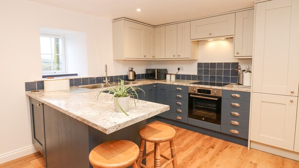 A modern kitchen with a large island, dark blue cabinets, and wooden stools. - The Byre (Hexham)